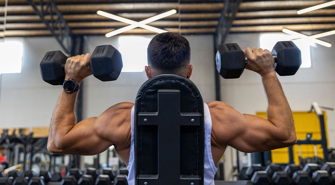 Home 14 Man with muscular anterior delt muscles performing a overhead dumbbell press at the gym